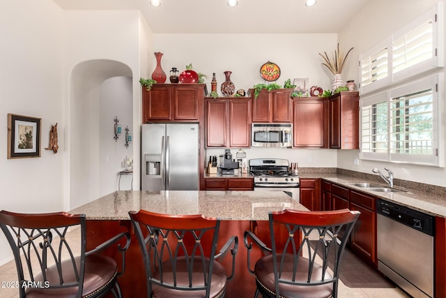 kitchen featuring a sink, light stone countertops, a kitchen island, and appliances with stainless steel finishes