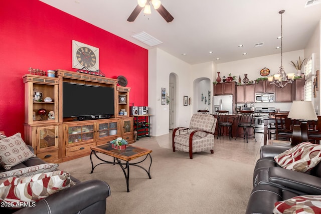 living room with ceiling fan with notable chandelier, visible vents, arched walkways, and light colored carpet