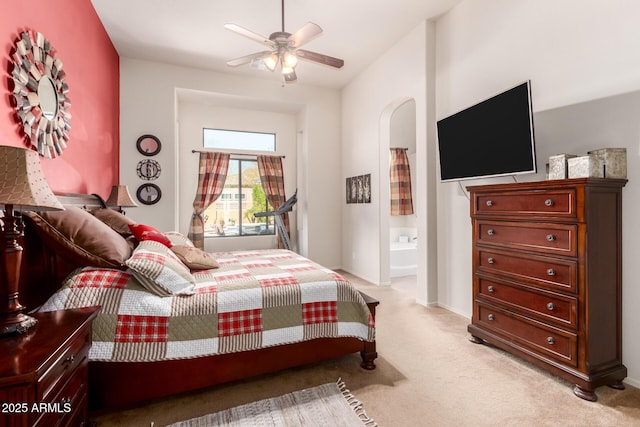 bedroom with baseboards, light carpet, arched walkways, and ensuite bath