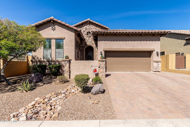 mediterranean / spanish-style home featuring stucco siding, a tile roof, decorative driveway, a fenced front yard, and a garage