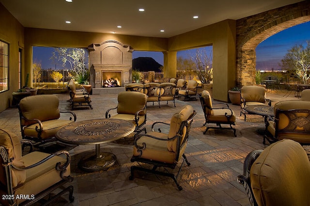 patio terrace at dusk with an outdoor living space with a fireplace and fence