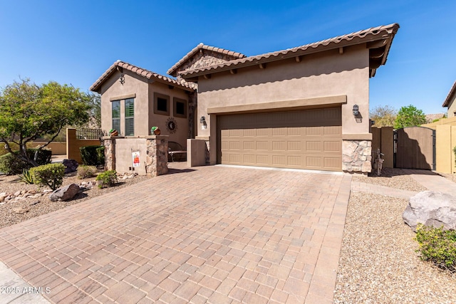 mediterranean / spanish-style house with decorative driveway, a gate, an attached garage, and stucco siding