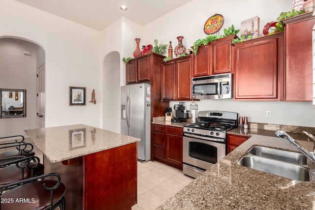 kitchen featuring dark stone countertops, a breakfast bar, arched walkways, a sink, and appliances with stainless steel finishes