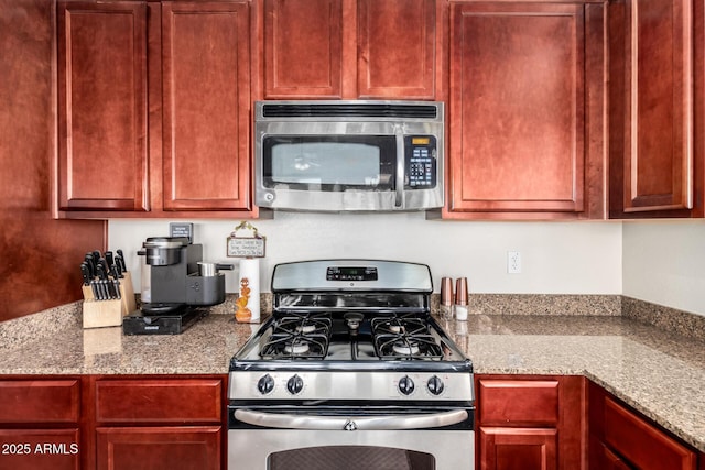 kitchen with stone counters, stainless steel appliances, and reddish brown cabinets