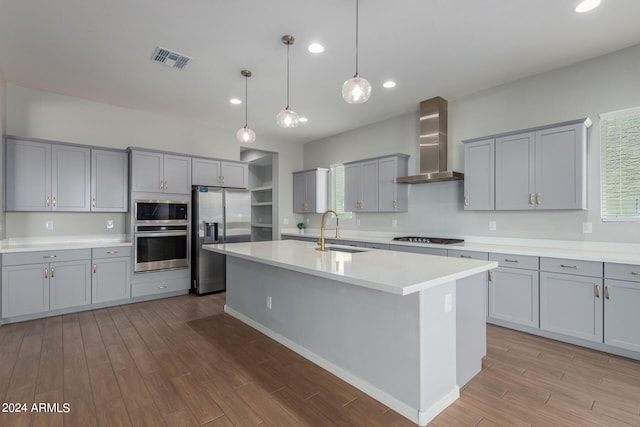 kitchen with wall chimney range hood, a wealth of natural light, a center island with sink, appliances with stainless steel finishes, and sink