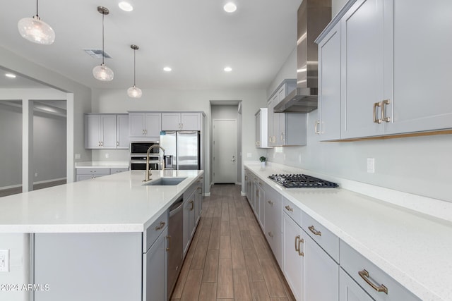 kitchen with hardwood / wood-style floors, stainless steel appliances, a center island with sink, hanging light fixtures, and wall chimney exhaust hood