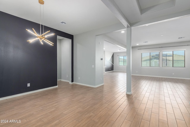 empty room featuring beamed ceiling, a chandelier, and light hardwood / wood-style flooring