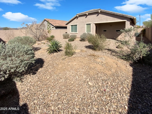 rear view of property featuring a tile roof, stucco siding, and fence private yard