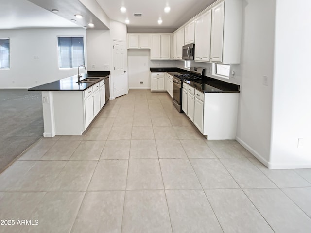 kitchen featuring dark countertops, light tile patterned floors, appliances with stainless steel finishes, and a sink