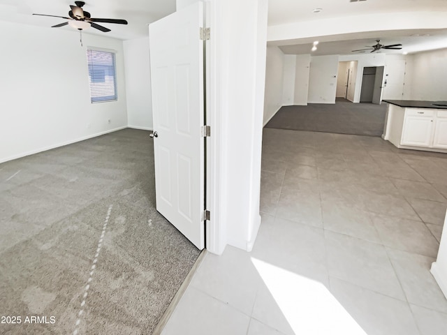 carpeted empty room featuring baseboards, a ceiling fan, and tile patterned flooring