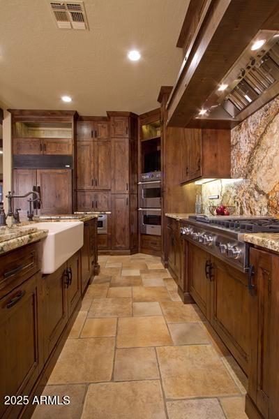 kitchen with visible vents, light stone countertops, range hood, appliances with stainless steel finishes, and a sink