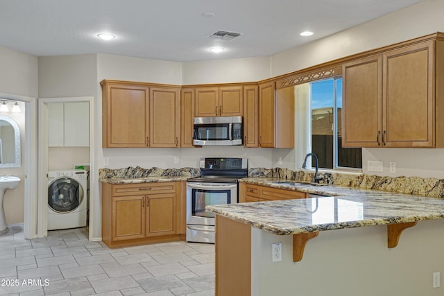 kitchen featuring visible vents, a peninsula, stainless steel appliances, washer / clothes dryer, and a sink