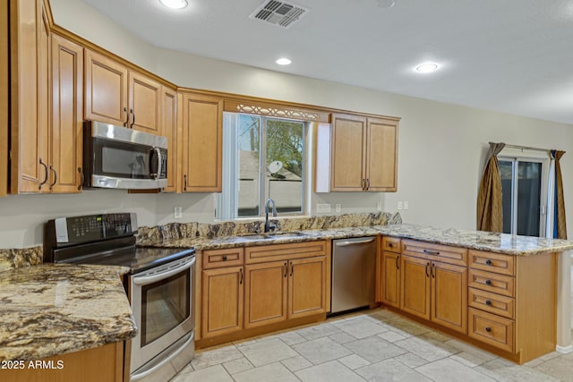 kitchen with visible vents, light stone counters, a peninsula, stainless steel appliances, and a sink