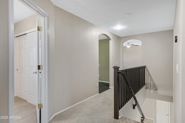 hallway with an upstairs landing, carpet, arched walkways, and baseboards