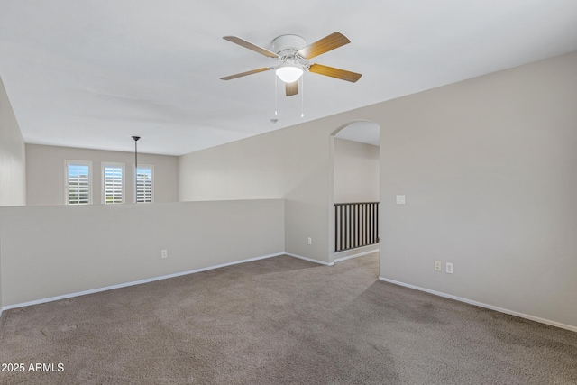 carpeted empty room with arched walkways, baseboards, and ceiling fan