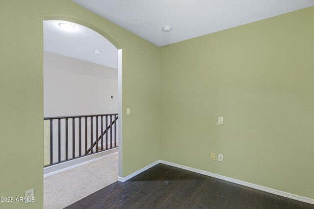 unfurnished room with baseboards, arched walkways, and dark wood-style flooring