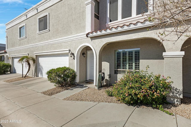 view of front of house with stucco siding, a garage, driveway, and a tiled roof