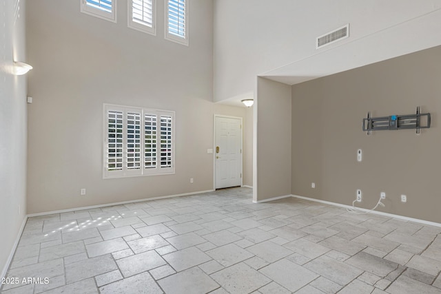 empty room with a high ceiling, baseboards, visible vents, and stone finish flooring