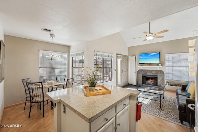 kitchen featuring hanging light fixtures, a textured ceiling, light hardwood / wood-style floors, a fireplace, and a kitchen island