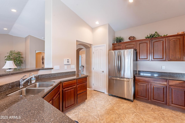 kitchen with dark stone counters, sink, stainless steel refrigerator, high vaulted ceiling, and light tile patterned floors