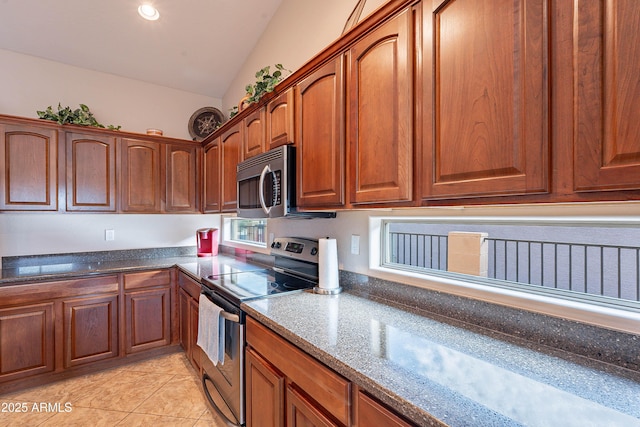 kitchen featuring vaulted ceiling, dark stone countertops, light tile patterned floors, and appliances with stainless steel finishes