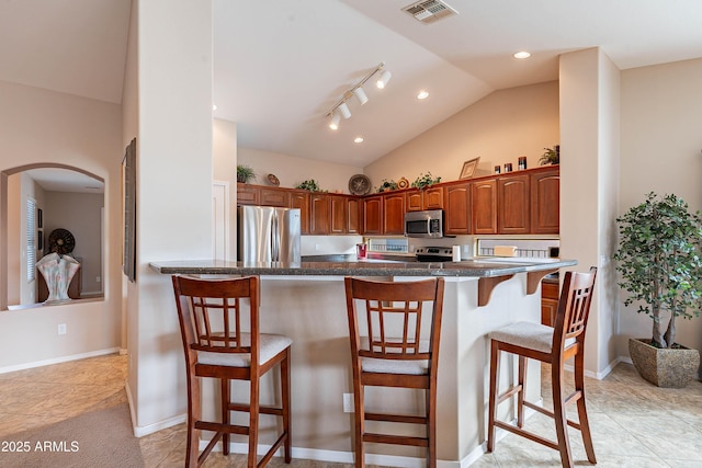 kitchen featuring a kitchen breakfast bar, light tile patterned flooring, vaulted ceiling, and appliances with stainless steel finishes