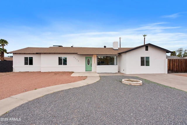 single story home featuring stucco siding, an outdoor fire pit, a shingled roof, and fence