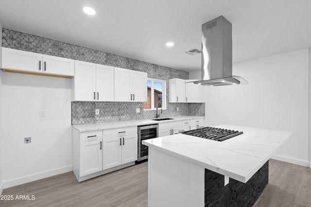 kitchen with visible vents, wine cooler, island range hood, white cabinets, and a sink