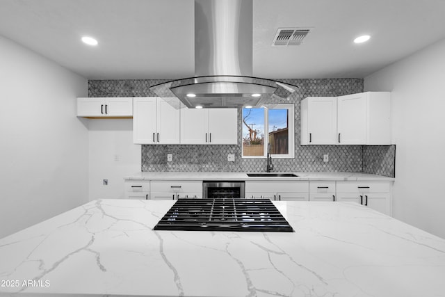 kitchen featuring visible vents, black gas stovetop, a sink, island exhaust hood, and tasteful backsplash