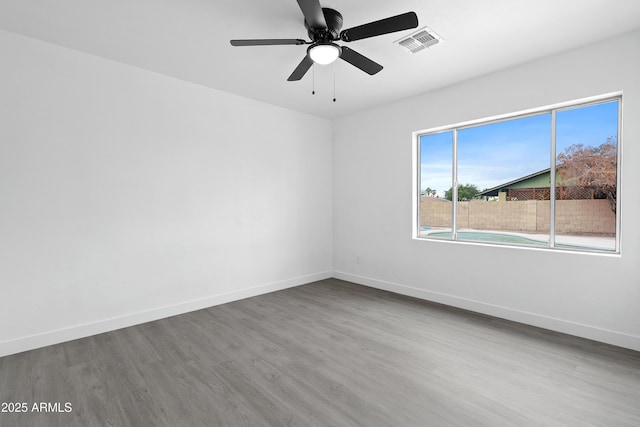 empty room featuring visible vents, a ceiling fan, baseboards, and wood finished floors