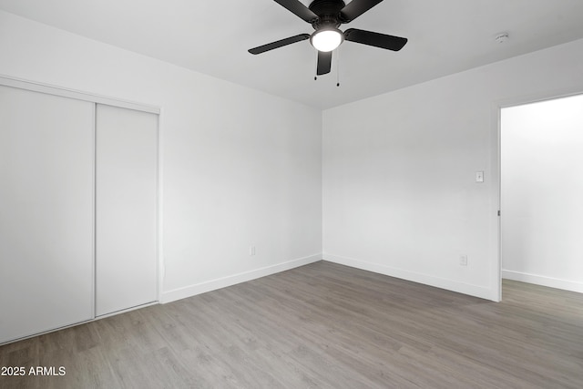 unfurnished bedroom featuring a ceiling fan, wood finished floors, baseboards, and a closet