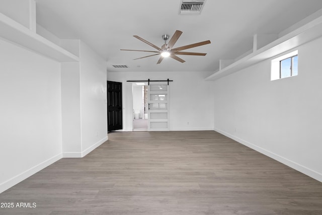 empty room featuring visible vents, a ceiling fan, a barn door, and wood finished floors