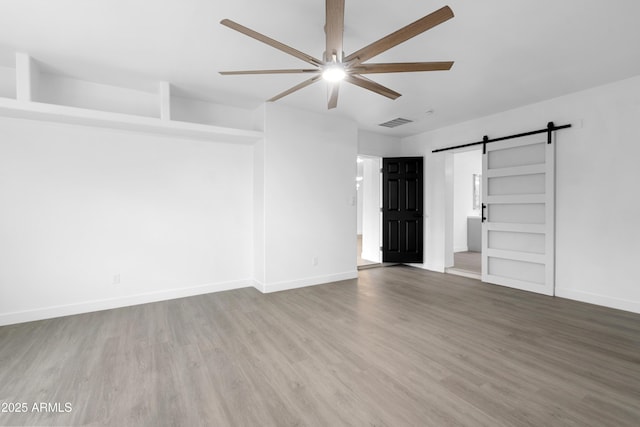 unfurnished room with visible vents, ceiling fan, baseboards, a barn door, and wood finished floors