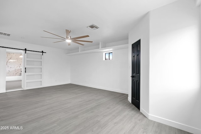 spare room featuring visible vents, ceiling fan, a barn door, and wood finished floors