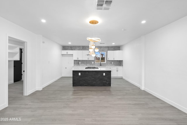 kitchen with a kitchen island, backsplash, light wood-style floors, white cabinets, and light countertops