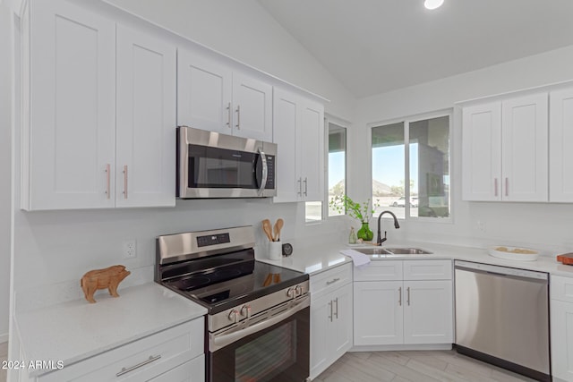 kitchen with sink, white cabinetry, stainless steel appliances, and vaulted ceiling