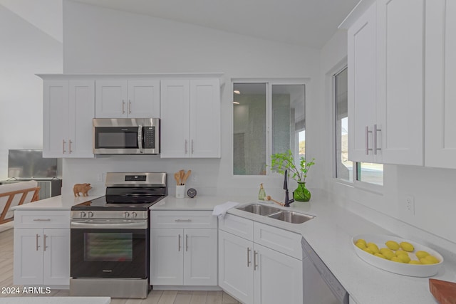 kitchen with white cabinets, sink, vaulted ceiling, light wood-type flooring, and appliances with stainless steel finishes