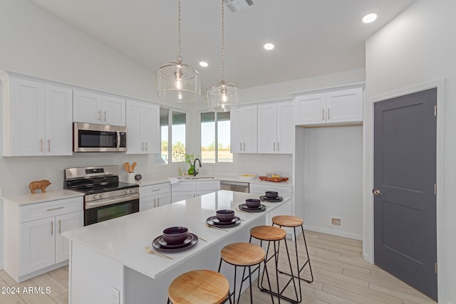 kitchen with white cabinetry, decorative light fixtures, vaulted ceiling, a kitchen island, and appliances with stainless steel finishes