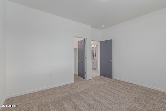 unfurnished bedroom with a walk in closet, a closet, and light colored carpet