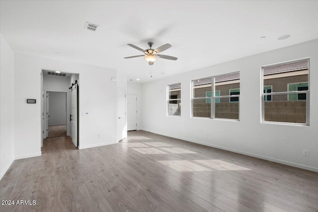 unfurnished room with light hardwood / wood-style flooring, a barn door, and ceiling fan