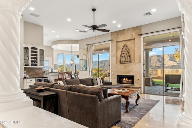 tiled living room with a tiled fireplace, ceiling fan, a mountain view, and ornate columns