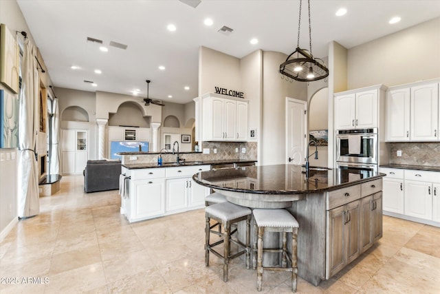 kitchen featuring white cabinetry, sink, dark stone countertops, a center island, and stainless steel double oven