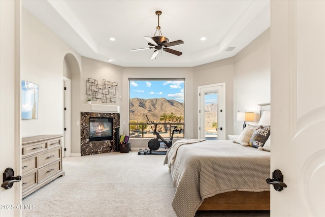 bedroom featuring a premium fireplace, a tray ceiling, a mountain view, access to outside, and light colored carpet