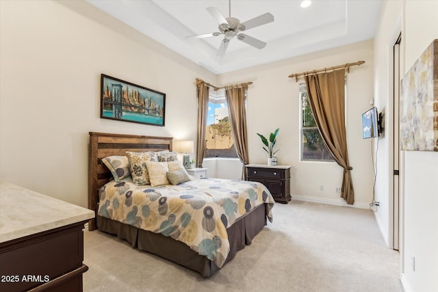 bedroom featuring ceiling fan, a tray ceiling, and light carpet