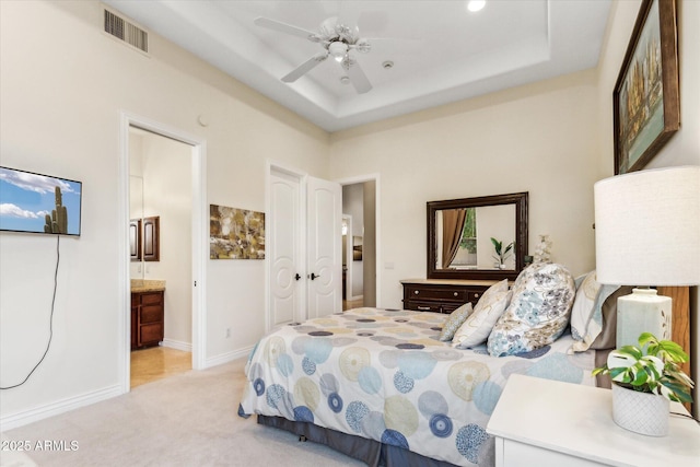 carpeted bedroom with a tray ceiling, ensuite bath, and ceiling fan