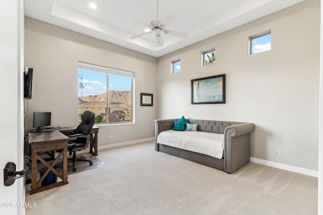 office featuring a tray ceiling, light colored carpet, and ceiling fan