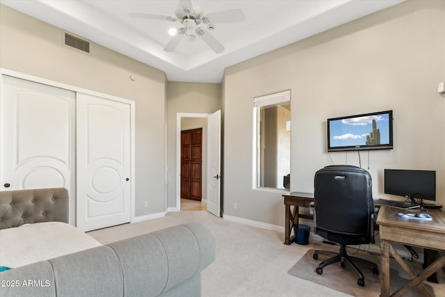 carpeted office space featuring ceiling fan and a raised ceiling