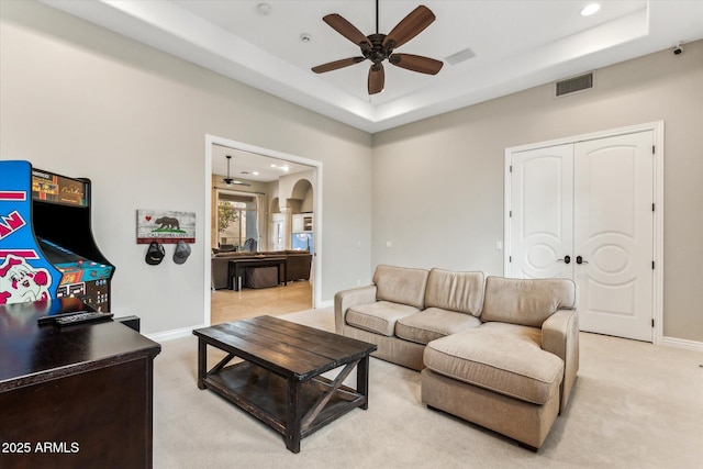 living room featuring ceiling fan, a tray ceiling, and light carpet