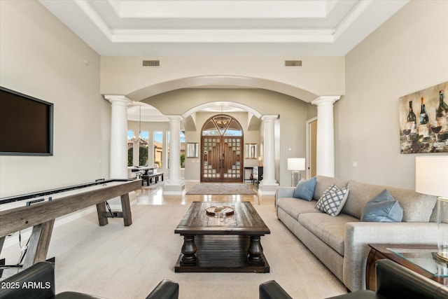 living room with a notable chandelier, a towering ceiling, a raised ceiling, and ornate columns