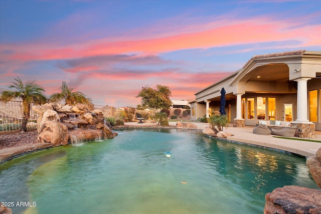 pool at dusk with a patio area and pool water feature